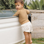 Toddler in a tan rash guard and Rylee & Cru Boys Swim Short in Race Car leaning on a stock tank pool