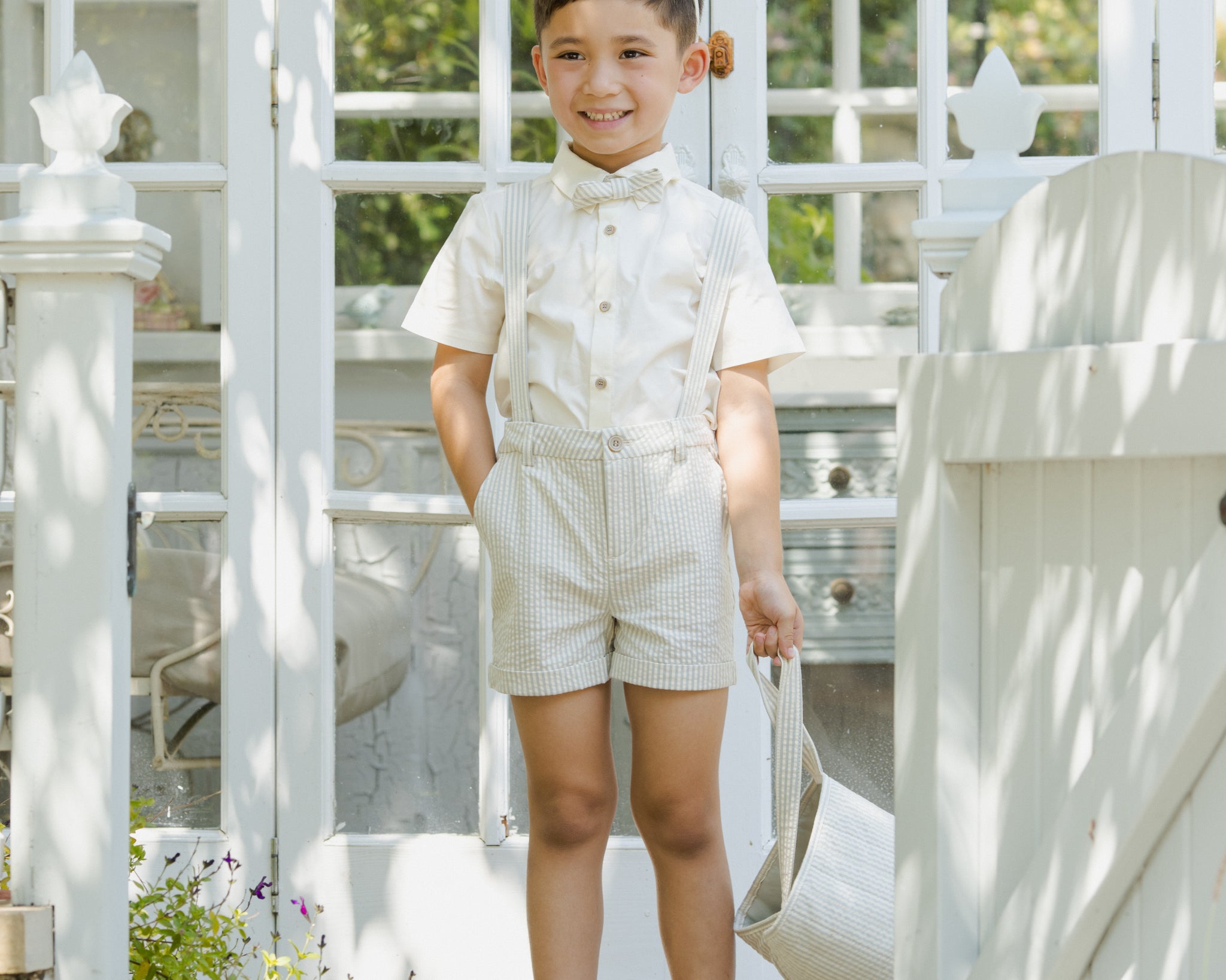 Boy in a cream shirt and shorts wearing a Rylee & Cru Bunny Headband by a garden gate
