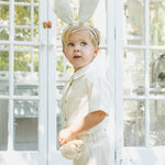 Boy in a white outfit wearing the Rylee & Cru Bunny Headband in Eucalyptus Check outside a greenhouse