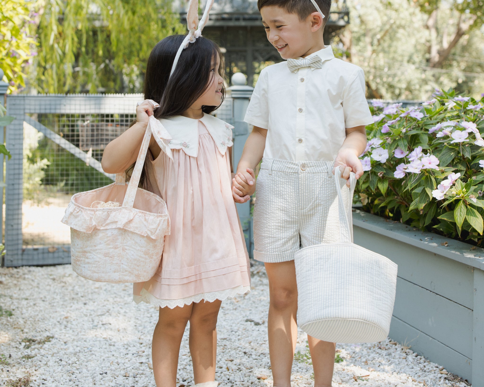 Girl and boy wearing Rylee & Cru Bunny Headbands carrying Easter baskets past raised garden beds