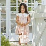 Girl in a pink dress wearing the Rylee & Cru Bunny Headband in Petal by a garden gate
