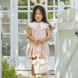 Girl in a pink dress wearing the Rylee & Cru Bunny Headband in Petal by a garden gate