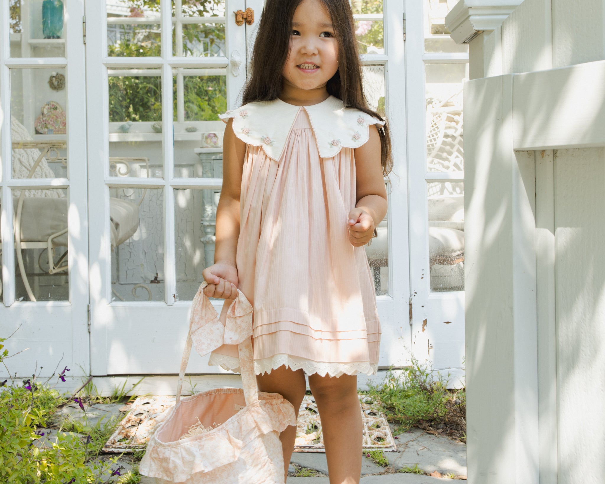 Girl in a pink dress wearing the Rylee & Cru Bunny Headband in Petal, holding a basket outside a greenhouse