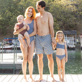 Parents holding a baby in the Rylee & Cru Chocolate Moxie One-Piece on a lake dock with their daughter