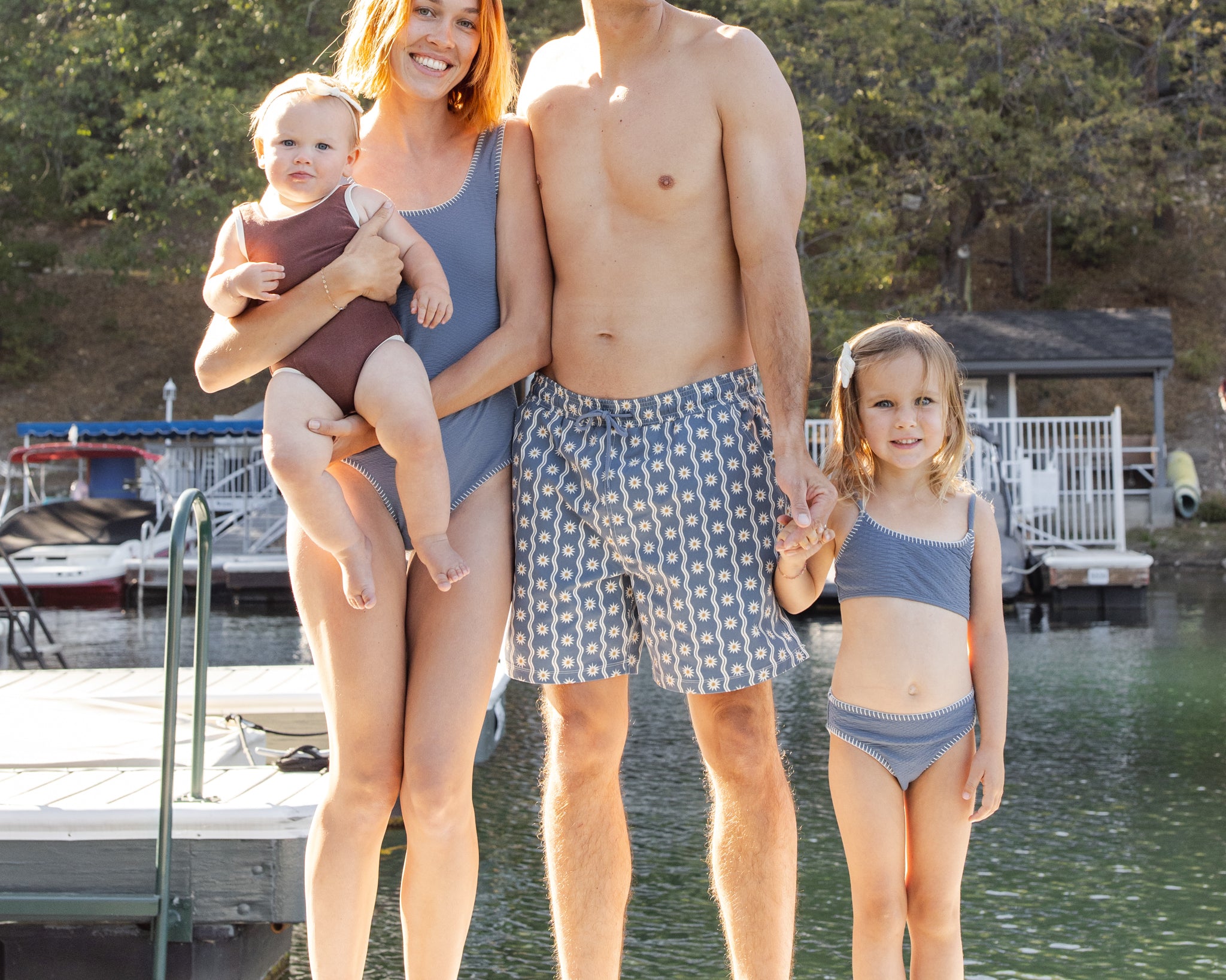 Family of four on a dock, baby in the Rylee & Cru Chocolate Moxie One-Piece, standing together by the water
