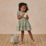 Girl in a sage green dress standing beside a Rylee & Cru Easter Basket on a wood floor