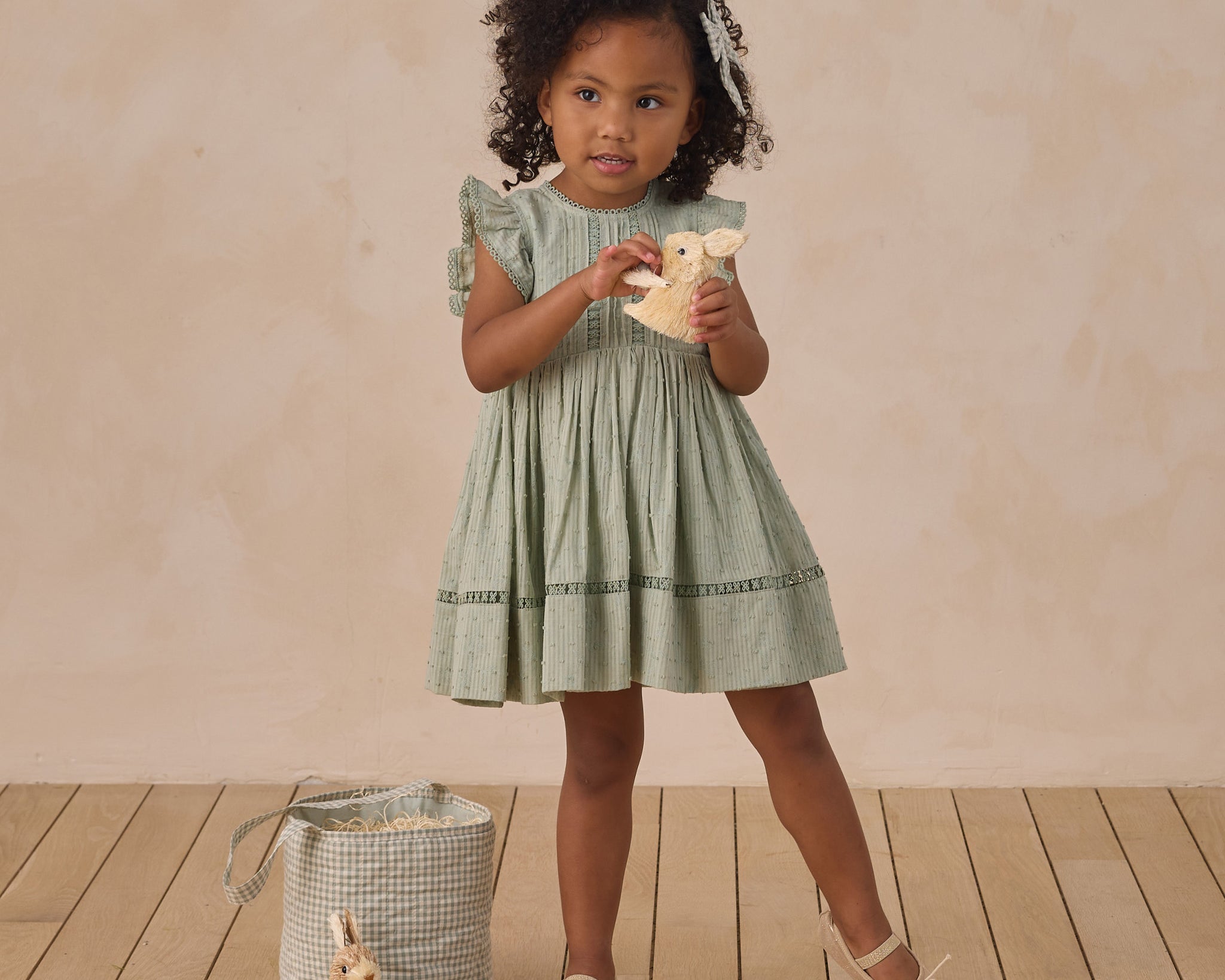 Girl in a sage green dress standing beside a Rylee & Cru Easter Basket on a wood floor