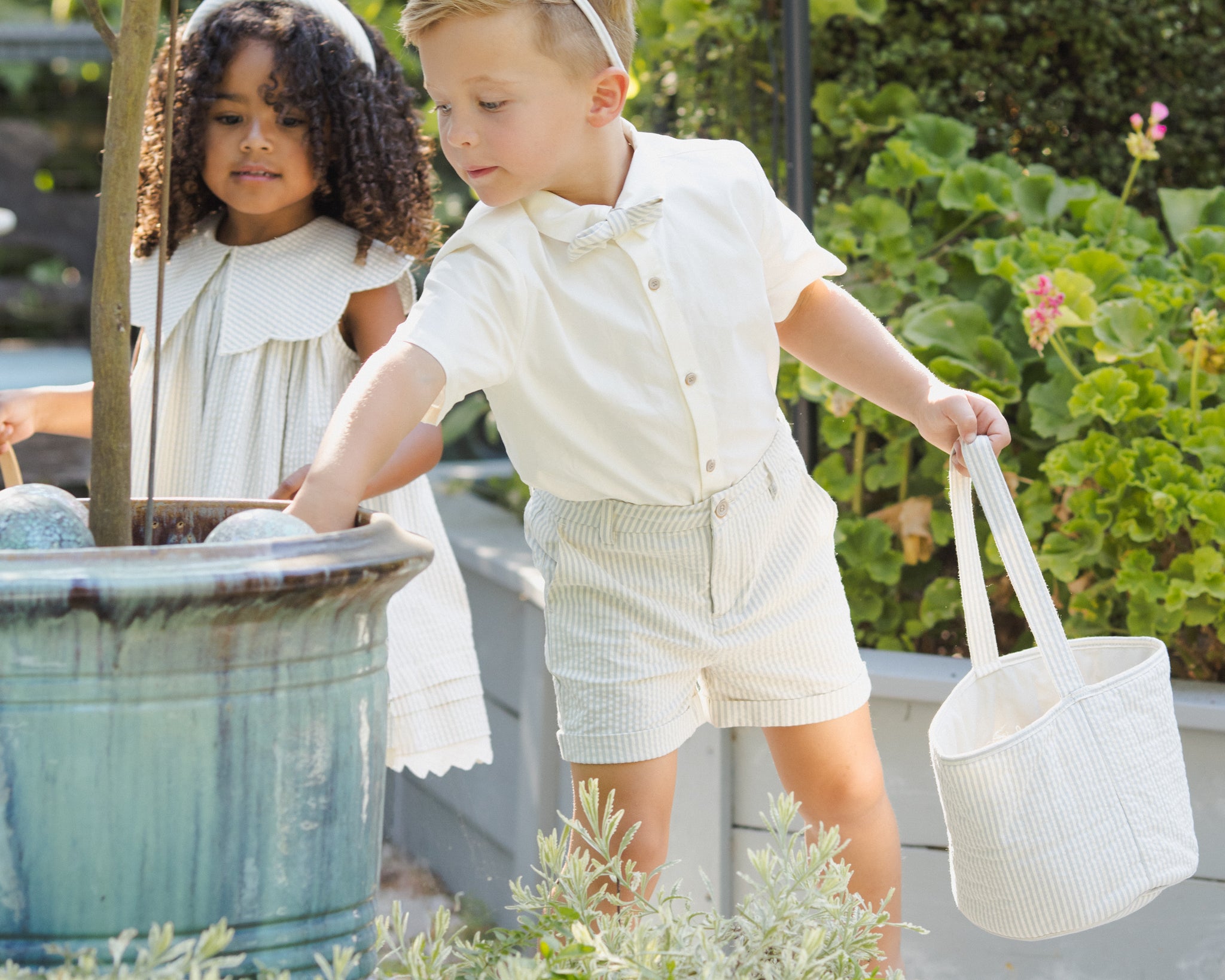 Two children in a garden with Rylee & Cru Easter Baskets in Sky Stripe and Eucalyptus Check