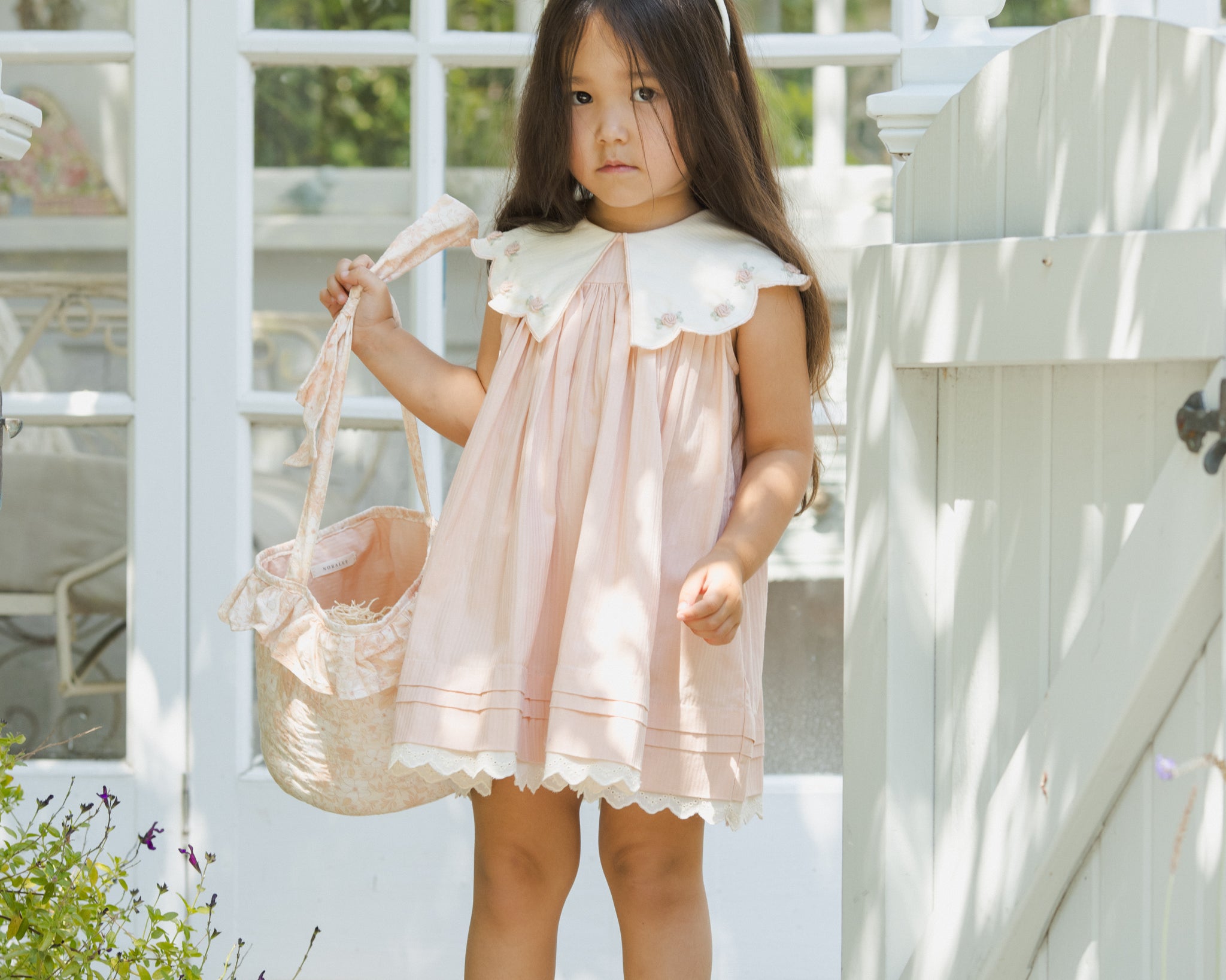 Girl in a pink dress and bunny ears holding the Rylee & Cru Easter Basket in Pastel Garden by a white gate