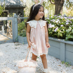 Girl in a pink dress carrying the Rylee & Cru Easter Basket in Pastel Garden through a garden path
