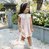 Girl in a pink dress carrying the Rylee & Cru Easter Basket in Pastel Garden through a garden path