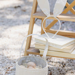 Rylee & Cru Easter Basket in Sky Stripe filled with eggs, sitting on gravel beside a stack of books and bunny ears