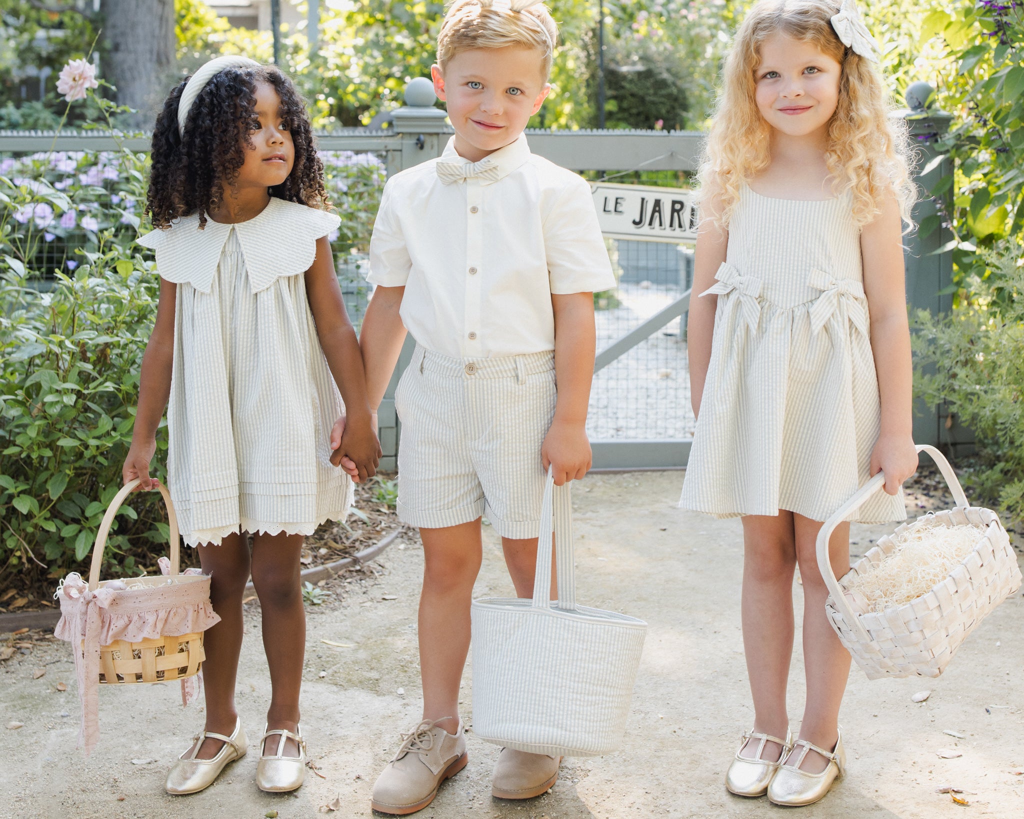 Three children in Easter outfits and bunny ears each holding a Rylee & Cru Easter Basket