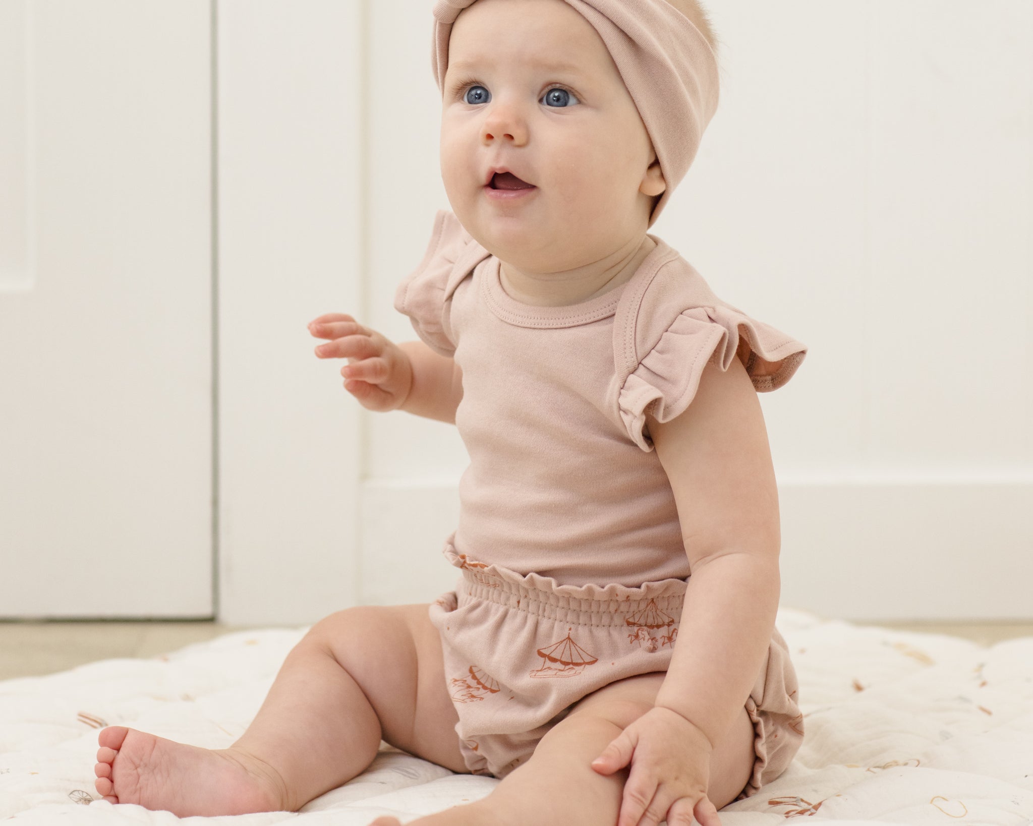 Baby in a pink turban headband sitting in the Rylee & Cru Flutter Sleeve Bodysuit in Blush with matching bloomers