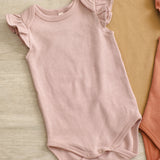 Rylee & Cru Flutter Sleeve Bodysuit in Blush laid beside Poppy and mustard bodysuits