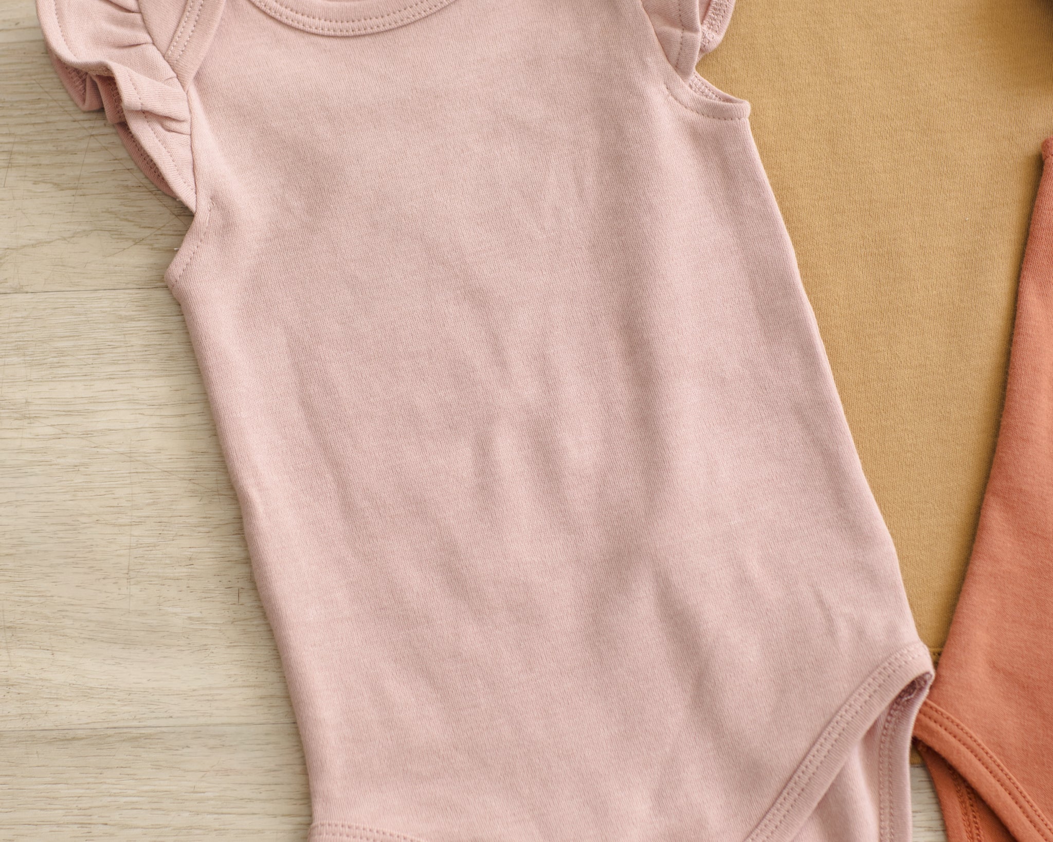 Rylee & Cru Flutter Sleeve Bodysuit in Blush laid beside Poppy and mustard bodysuits