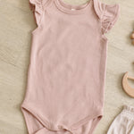 Rylee & Cru Flutter Sleeve Bodysuit in Blush laid on a wood floor with a wooden toy