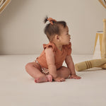 Baby looking to the side wearing the Rylee & Cru Flutter Sleeve Bodysuit in Poppy