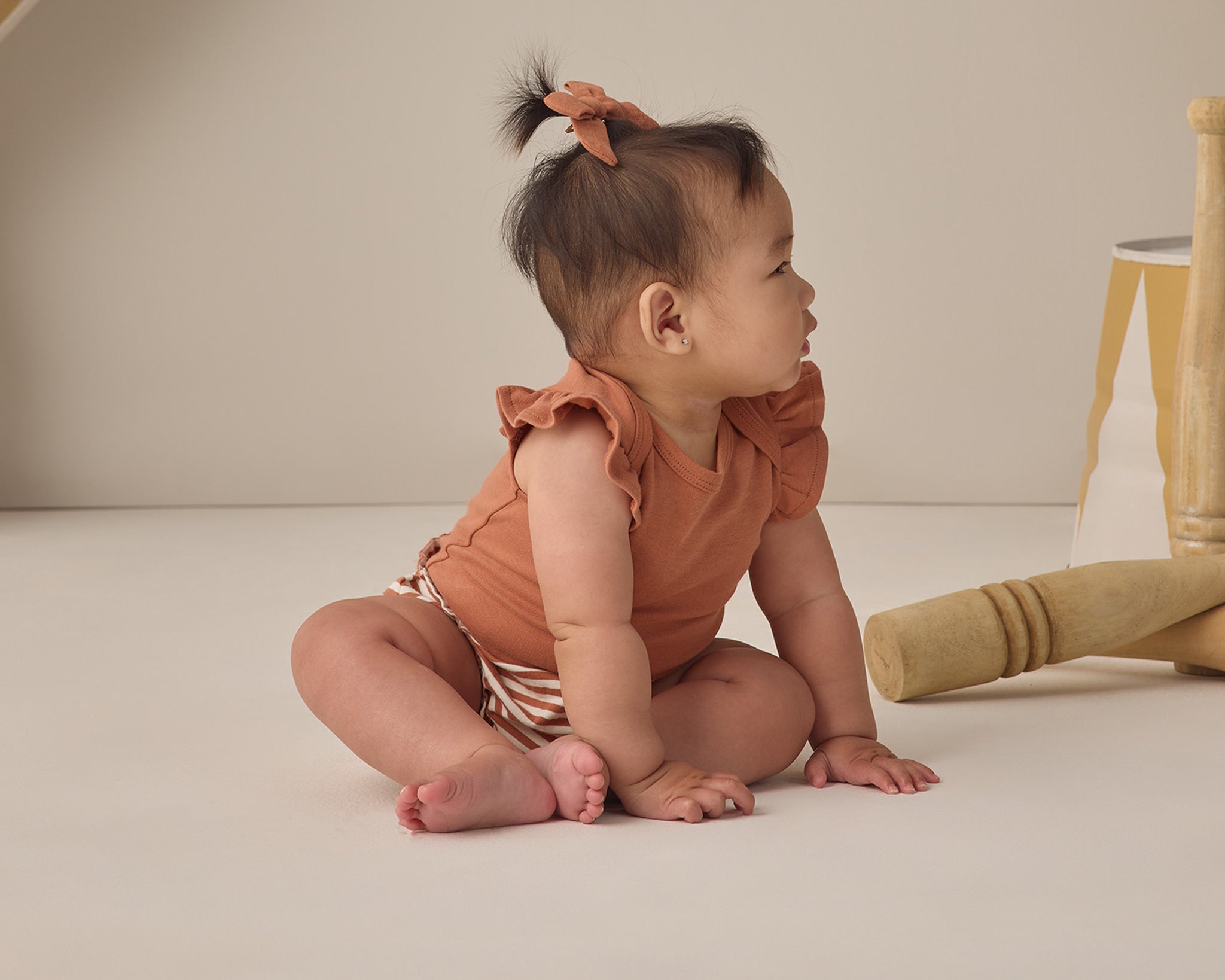Baby looking to the side wearing the Rylee & Cru Flutter Sleeve Bodysuit in Poppy