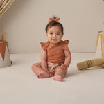 Smiling baby in the Rylee & Cru Flutter Sleeve Bodysuit in Poppy sitting on a cream backdrop