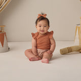 Smiling baby in the Rylee & Cru Flutter Sleeve Bodysuit in Poppy sitting on a cream backdrop