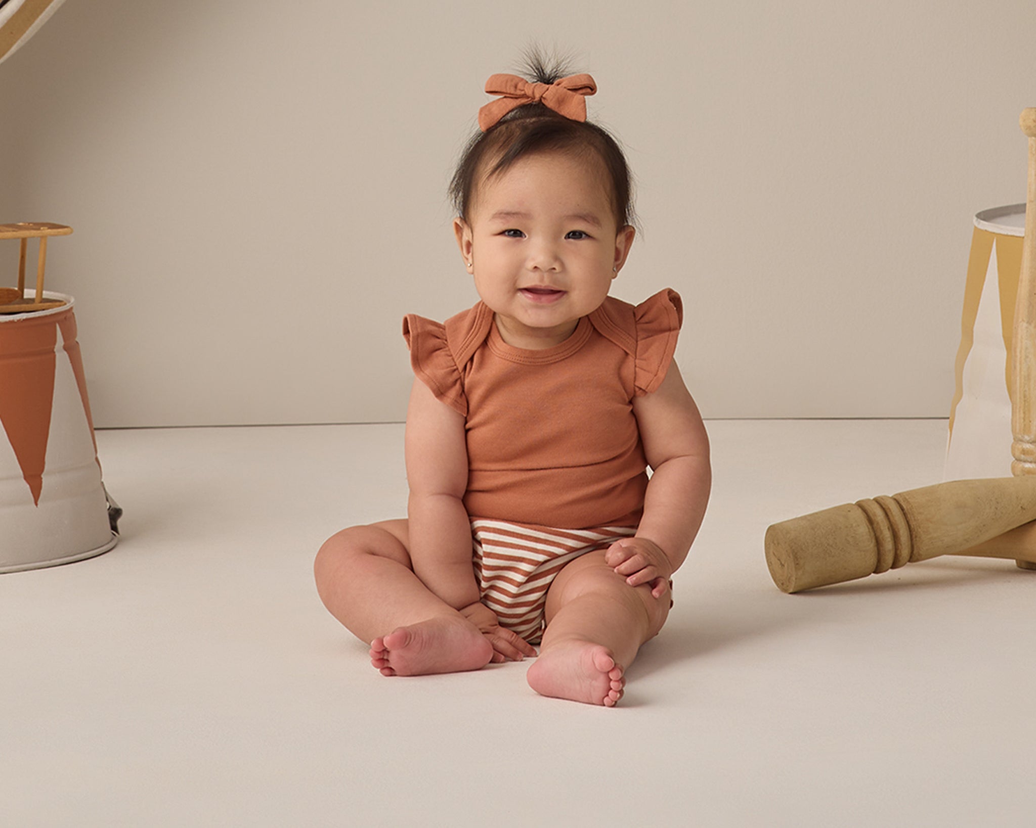 Smiling baby in the Rylee & Cru Flutter Sleeve Bodysuit in Poppy sitting on a cream backdrop