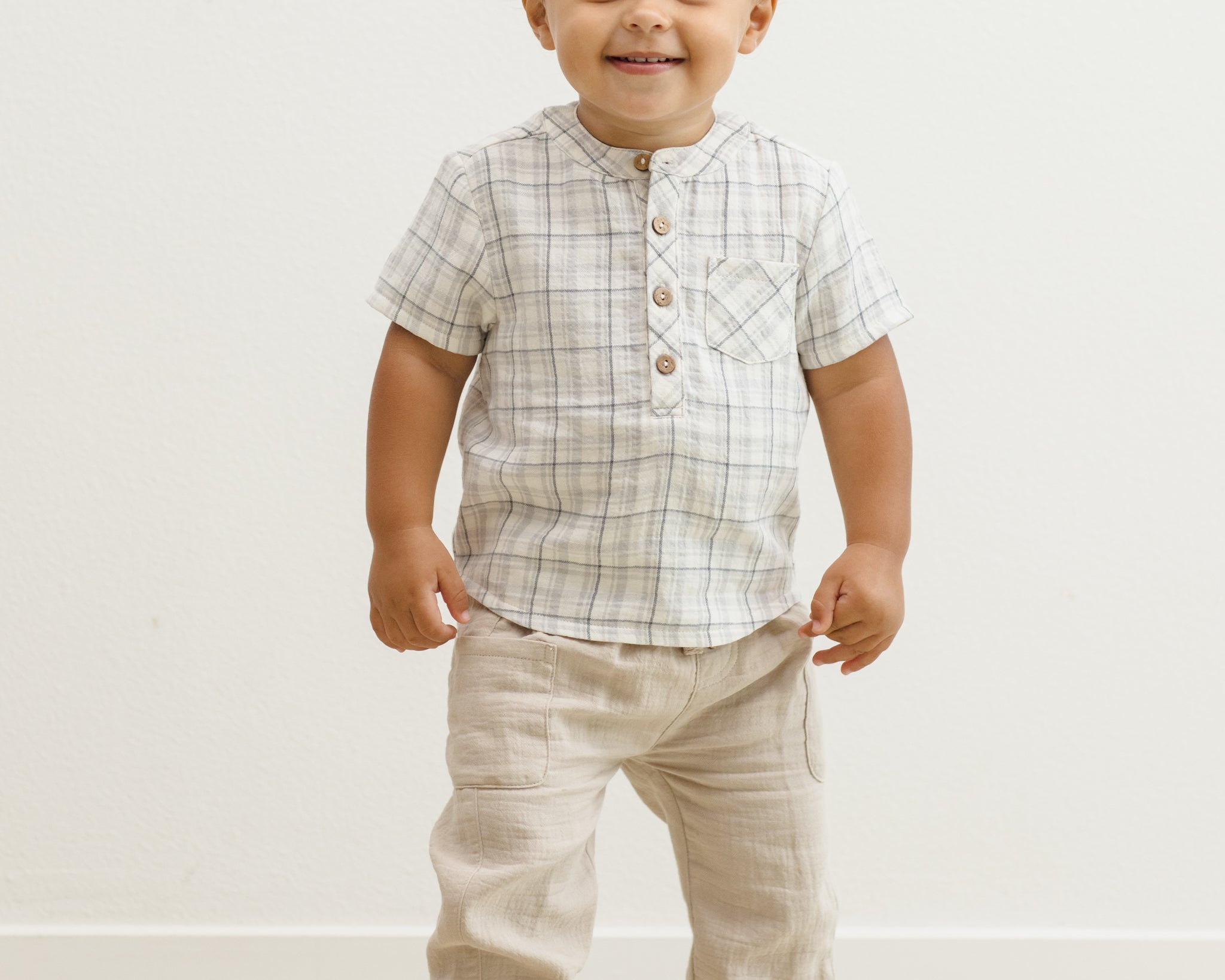 Smiling toddler facing forward in the Rylee & Cru Jaxson Shirt in Blue Plaid and tan pants