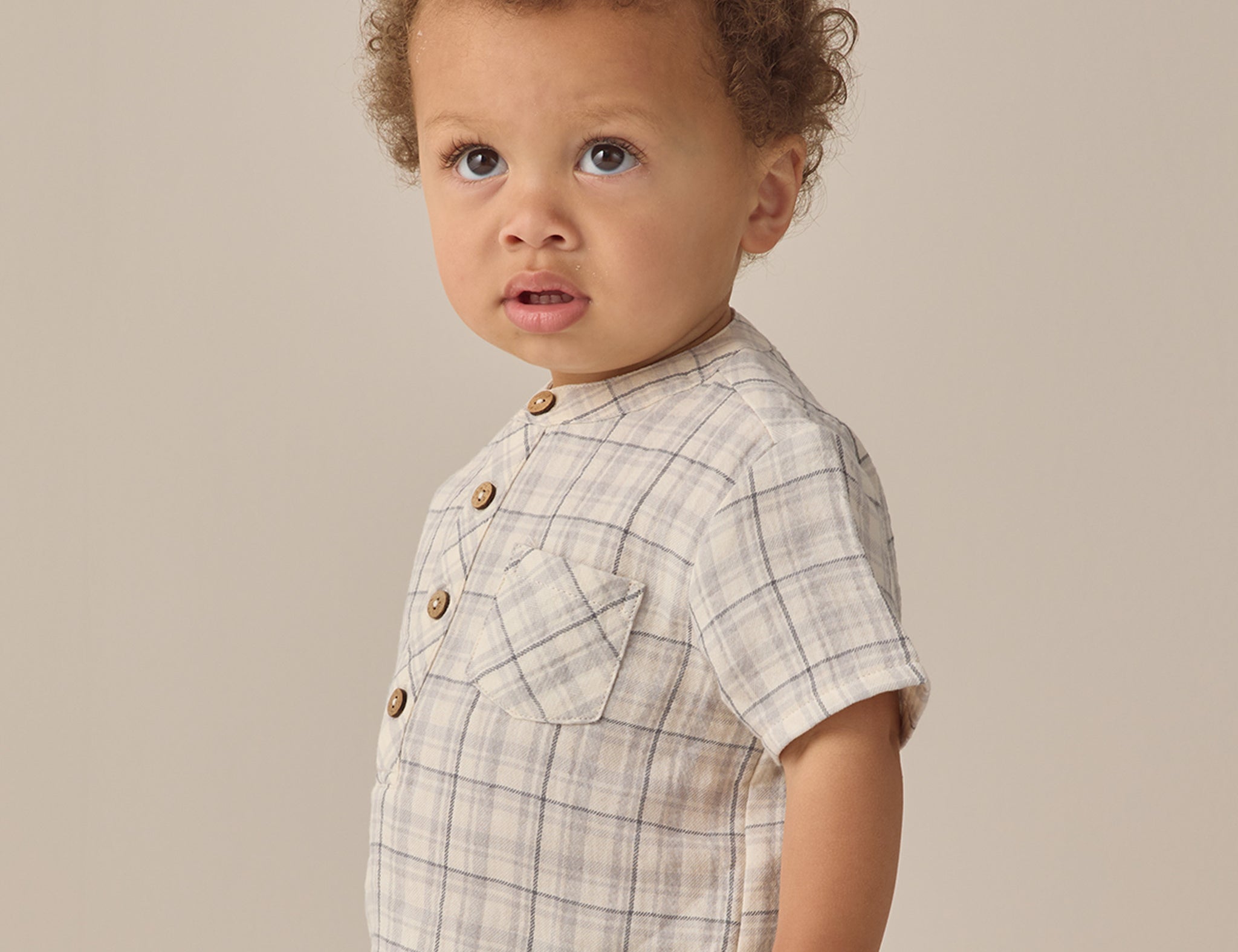 Toddler with curly hair wearing the Rylee & Cru Jaxson Shirt in Blue Plaid, side view