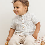 Toddler sitting on a rattan bench wearing the Rylee & Cru Jaxson Shirt in Blue Plaid