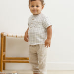 Toddler standing beside a rattan chair in the Rylee & Cru Jaxson Shirt in Blue Plaid and tan pants