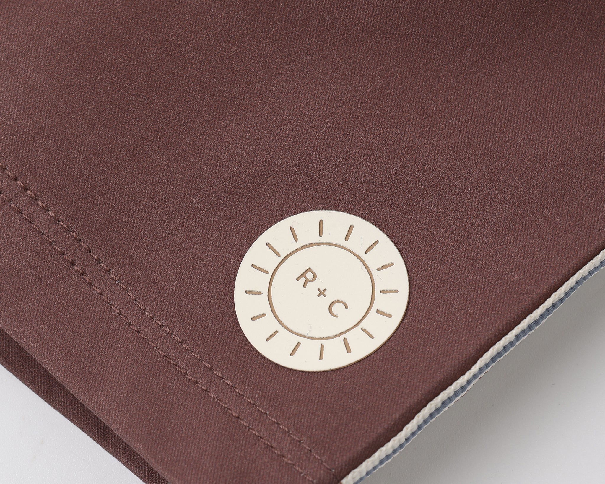 Close-up of the R+C sun logo patch on the Rylee & Cru Paneled Boardshort in Chocolate