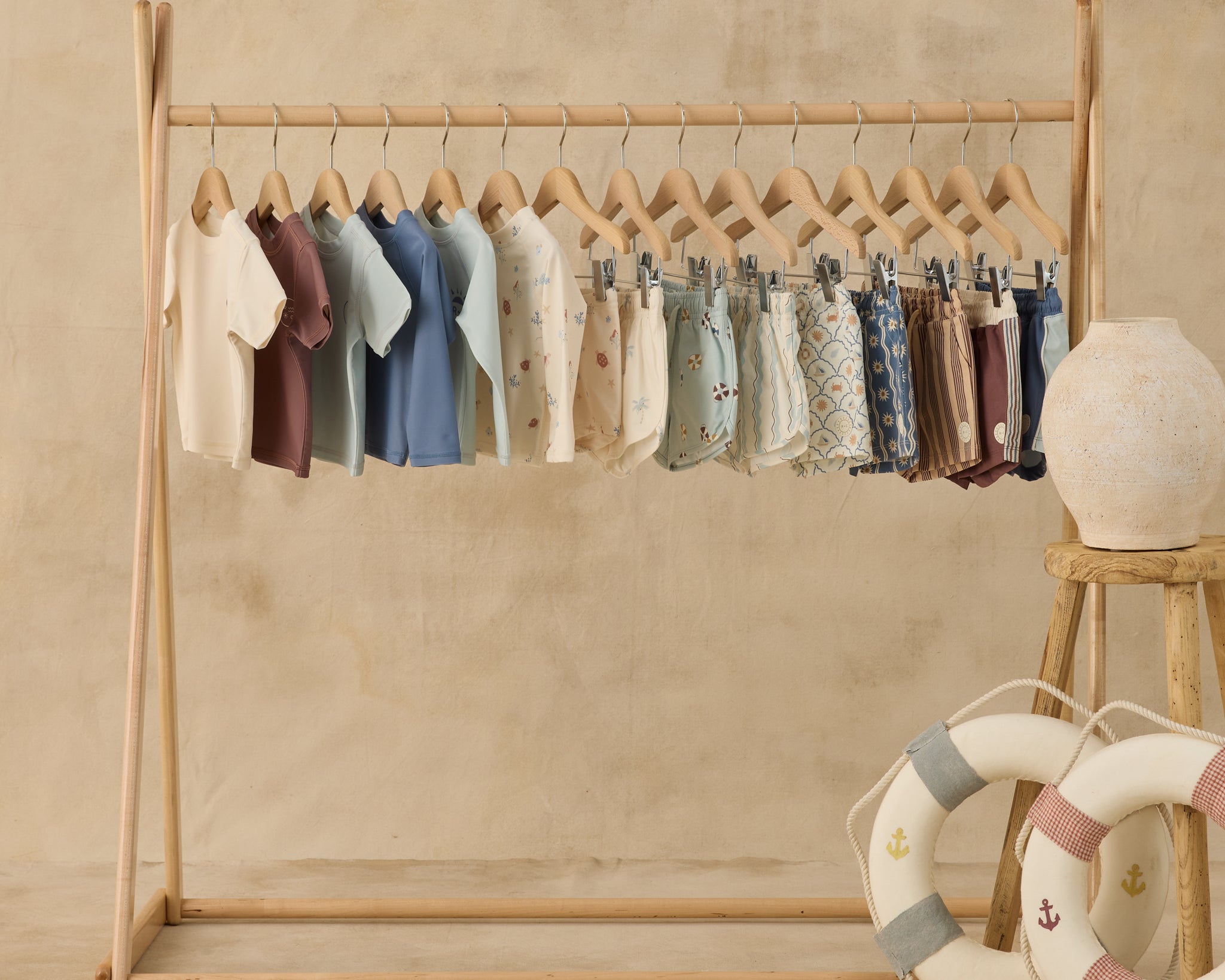 Rylee & Cru swim collection on a wooden rack with toy life rings, Paneled Boardshorts included