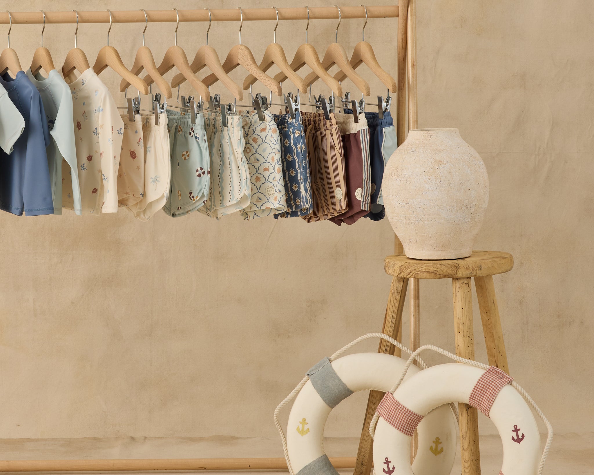 Rylee & Cru swim collection hanging on a wooden rack with a toy life ring, Paneled Boardshorts included