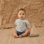 Baby in a Meet Me at the Beach tee and Rylee & Cru Paneled Boardshort in Marine sitting with a toy sailboat