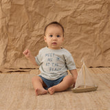 Baby in a Meet Me at the Beach tee and Rylee & Cru Paneled Boardshort in Marine sitting with a toy sailboat