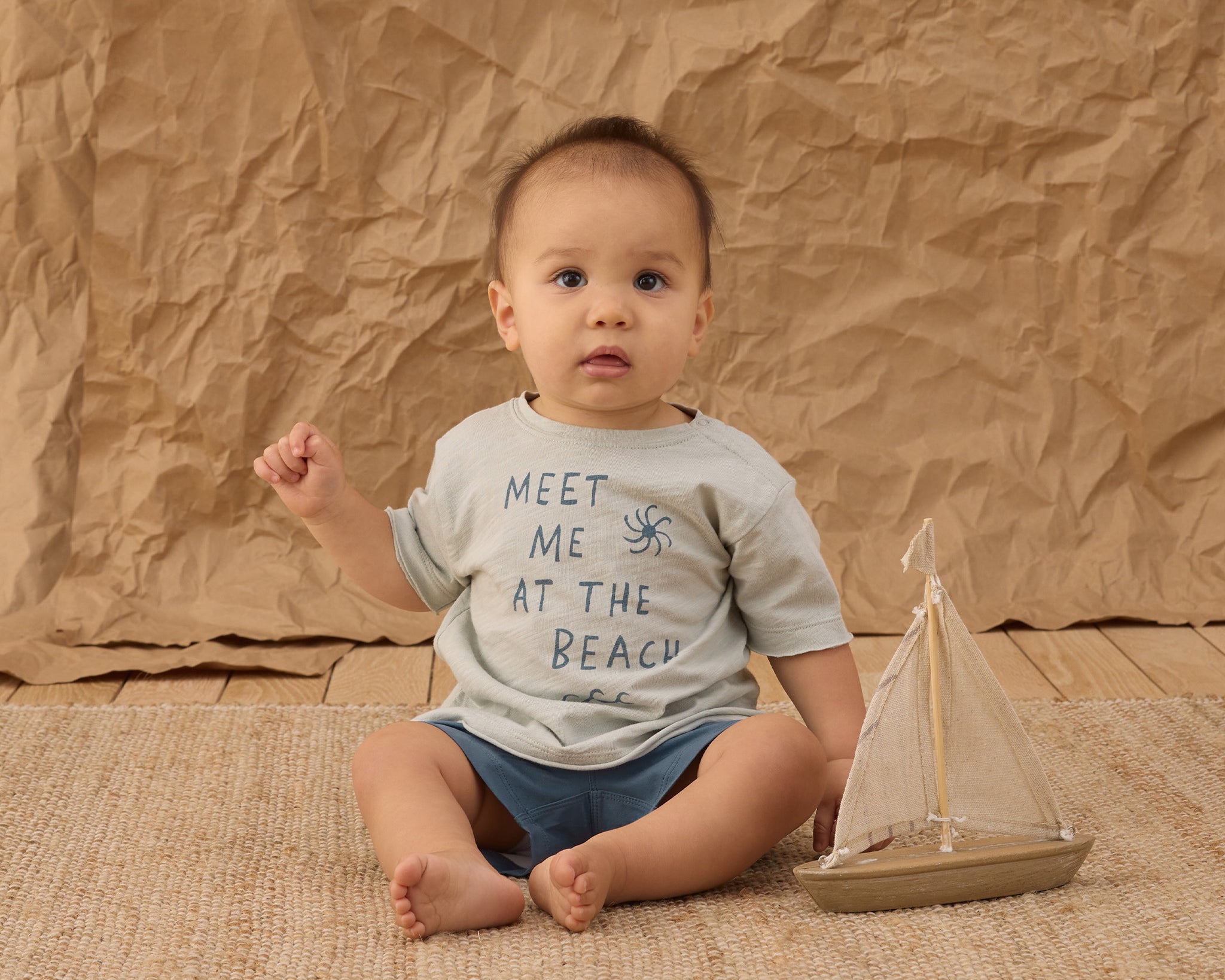 Baby in a Meet Me at the Beach tee and Rylee & Cru Paneled Boardshort in Marine sitting with a toy sailboat