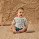 Baby sitting on a jute rug wearing the Rylee & Cru Paneled Boardshort in Marine with a beach tee