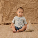 Baby sitting on a jute rug wearing the Rylee & Cru Paneled Boardshort in Marine with a beach tee