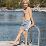 Boy on a lake dock ladder wearing the Rylee & Cru Paneled Boardshort in Marine