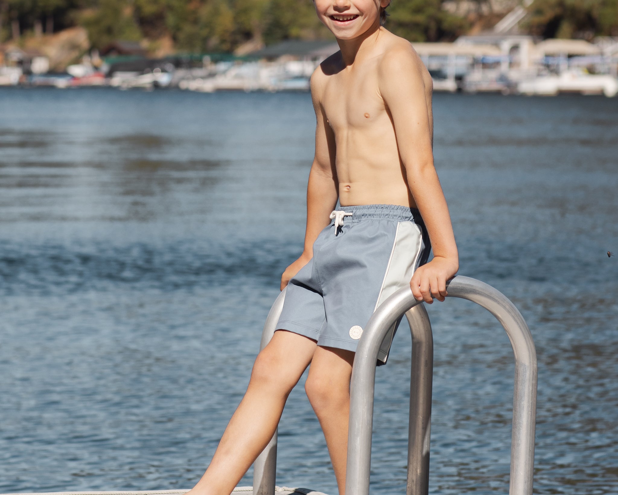 Boy on a lake dock ladder wearing the Rylee & Cru Paneled Boardshort in Marine
