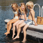 Kids sitting on a lake dock with their feet in the water, one in the Rylee & Cru Paneled Boardshort in Marine
