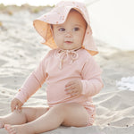 Baby in a floral sun bonnet sitting on the sand wearing the Rylee & Cru Rashguard Long Sleeve in Blush