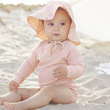 Baby in a floral sun bonnet sitting on the sand wearing the Rylee & Cru Rashguard Long Sleeve in Blush