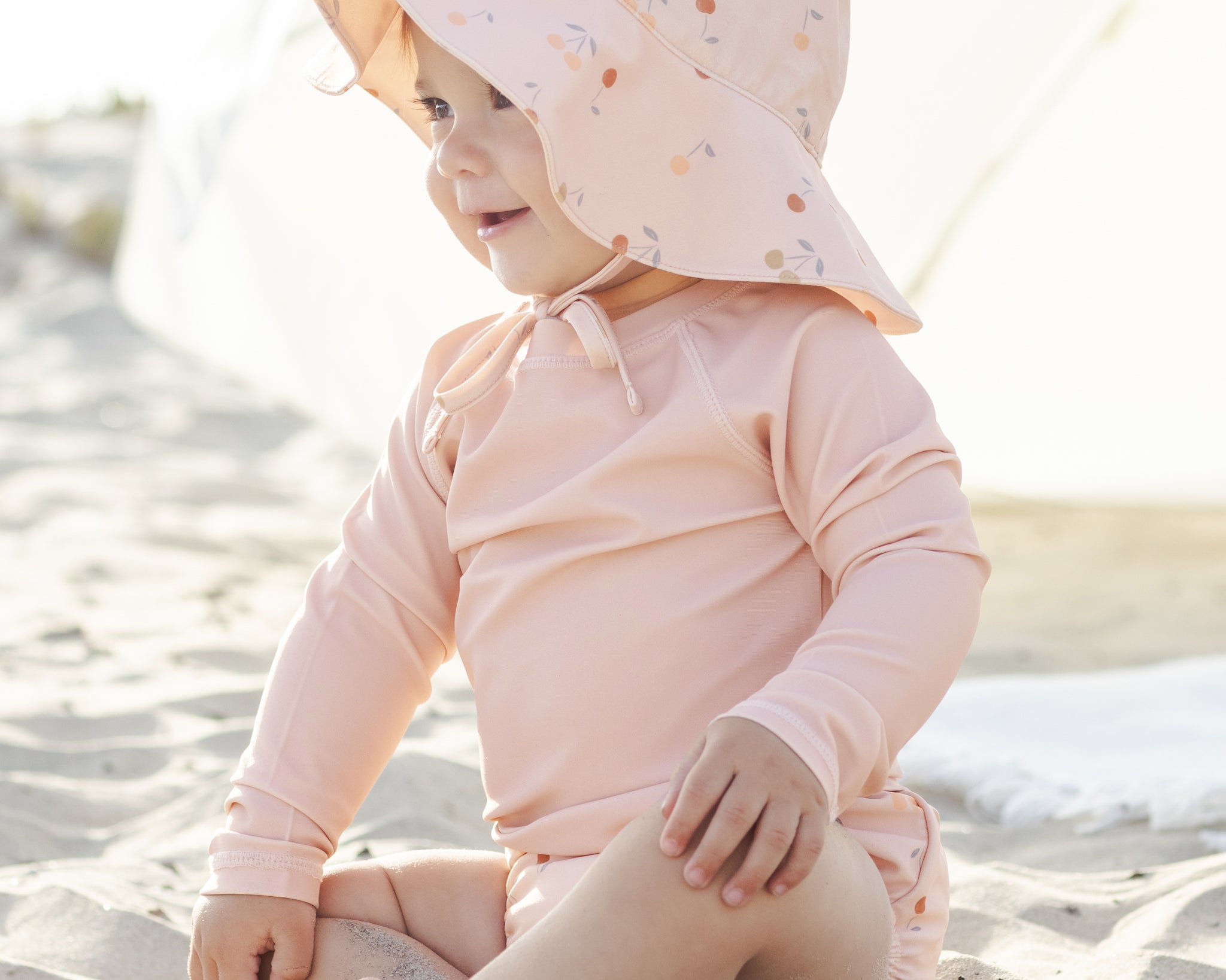 Baby in a sun bonnet playing on the beach in the Rylee & Cru Rashguard Long Sleeve in Blush
