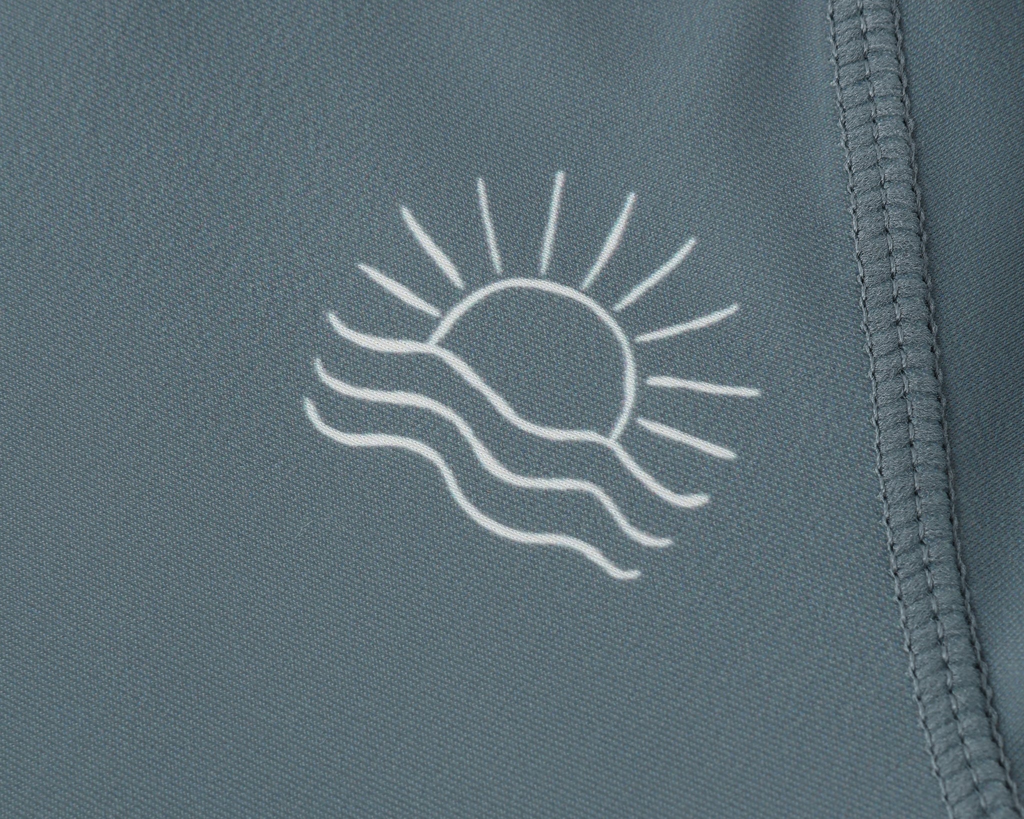 Close-up of the embroidered sun and wave logo on the Rylee & Cru Rashguard Long Sleeve in Ocean