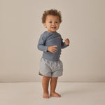Smiling toddler standing in the Rylee & Cru Rashguard Long Sleeve in Ocean with gingham trunks