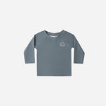 Rylee & Cru Rashguard Long Sleeve in Ocean, a slate blue baby swim top with a small sun logo, laid flat