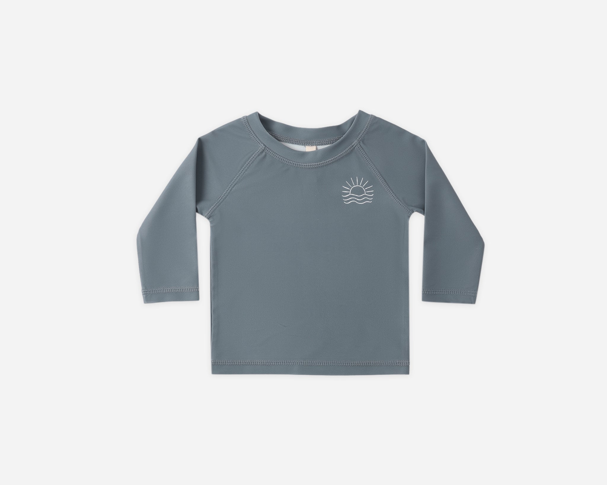 Rylee & Cru Rashguard Long Sleeve in Ocean, a slate blue baby swim top with a small sun logo, laid flat