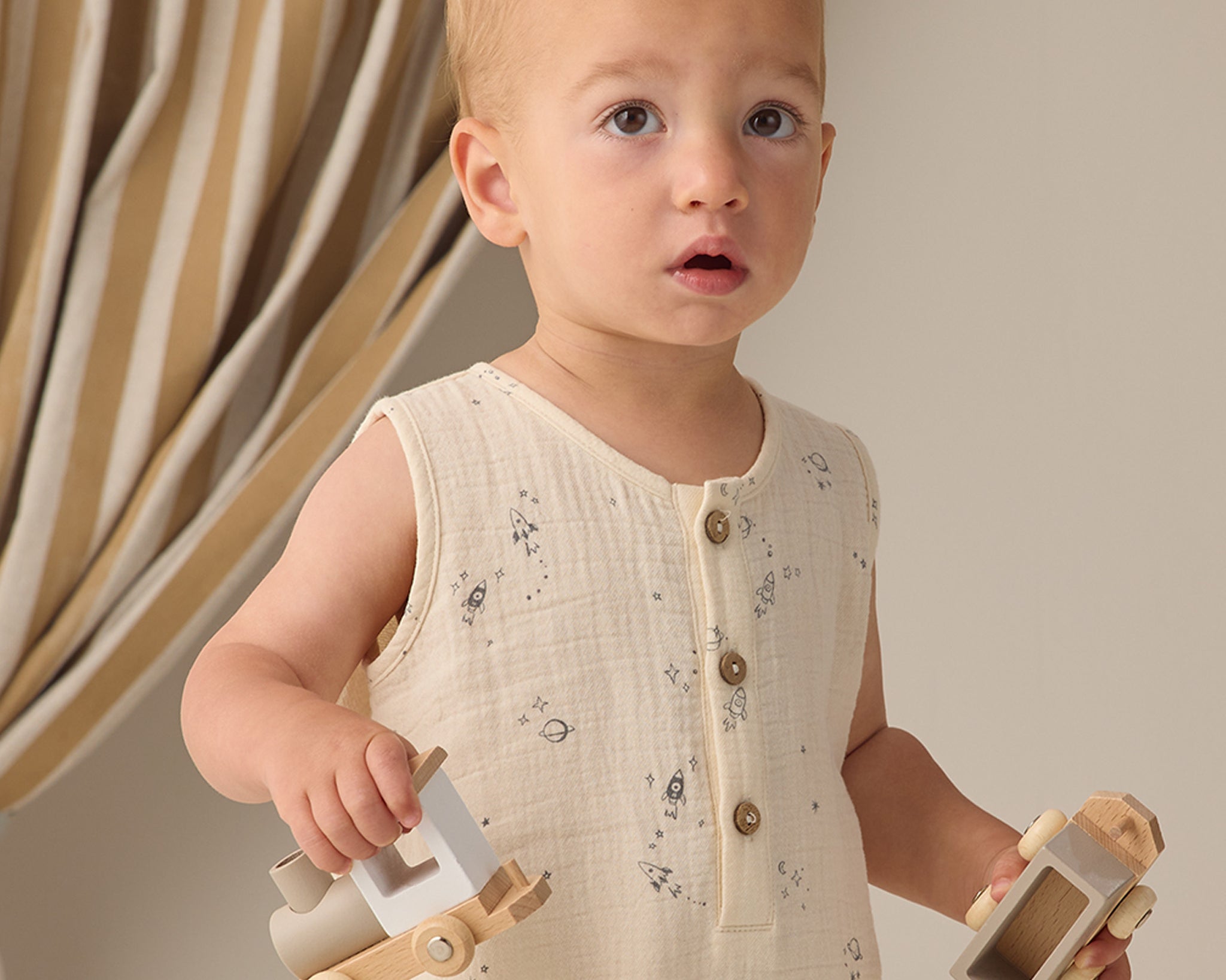 Toddler holding wooden toy cars while wearing the Rylee & Cru Romper in Space