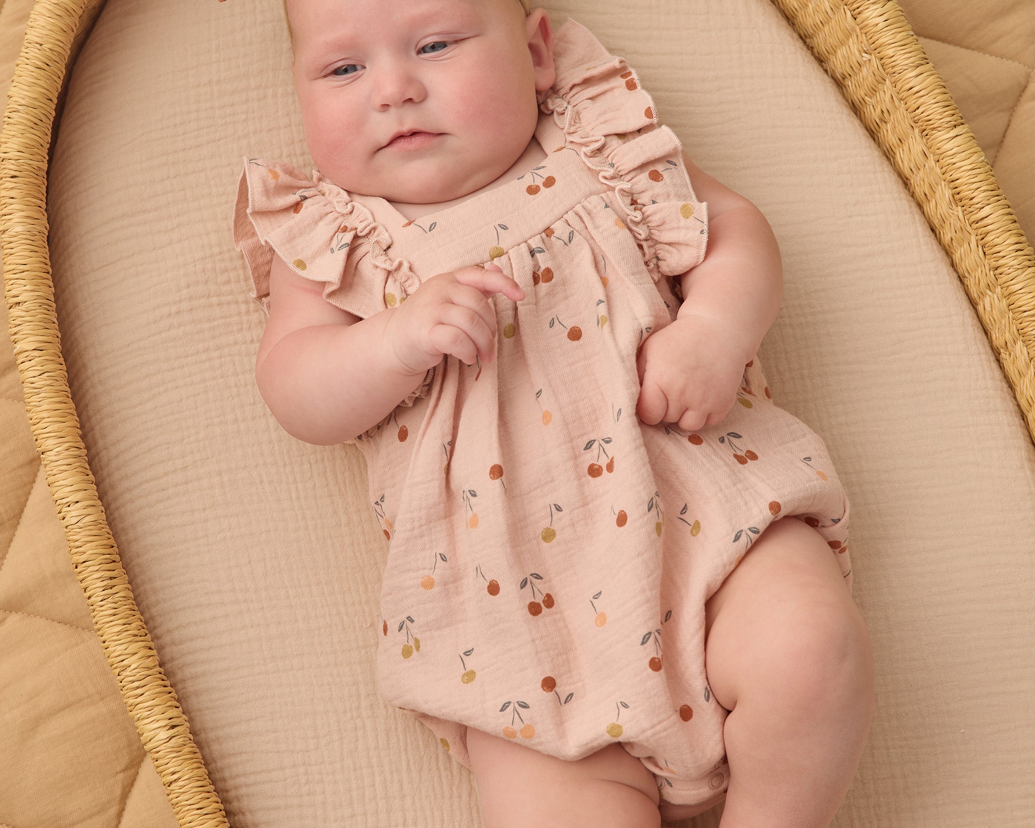 Baby with a bow headband lying in a wicker bassinet wearing the Rylee & Cru Ruffle Romper in Cherries